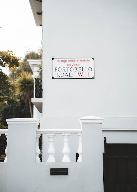 A close-up view of a white residential building during a house removal process, showing a white-painted exterior wall with a street sign reading 'Portobello Road, W11,' indicating the location in Chel