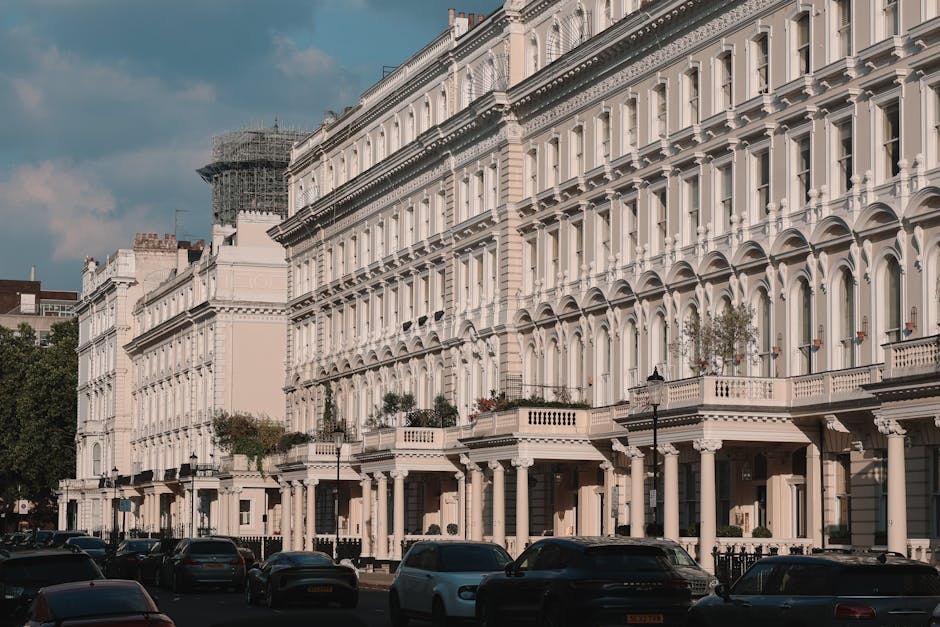 Photograph of a typical Chelsea terrace building with multiple floors and large sash windows. The building's facade features a mix of brickwork and decorative white stucco accents around the windows and doorway. Several small balconies with ornate black wrought iron railings extend from the upper floors, with potted plants and small trees placed on the balconies. The scene is illuminated by natural daylight, with clear blue skies in the background. The image captures the exterior of the property, illustrating an urban residential environment suitable for house removals or home relocation services. Man and a Van Chelsea often assist with packing, furniture transport, and loading processes, which are part of organized moves involving these types of historic terrace buildings.