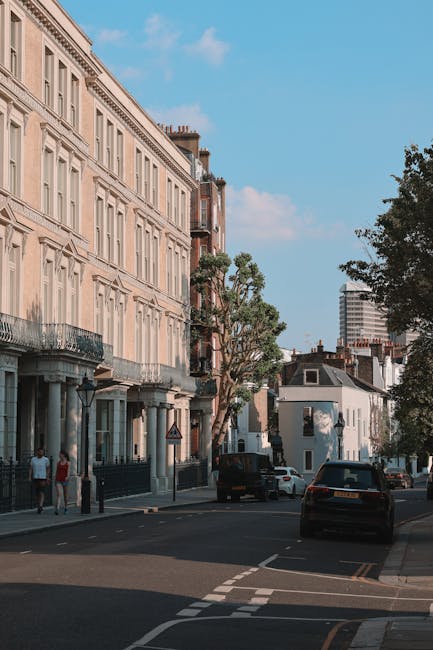 A wide shot of a multi-storey white residential building with classical architectural features, including decorative cornices, wrought iron balconies, and large sash windows, situated along a tree-lin